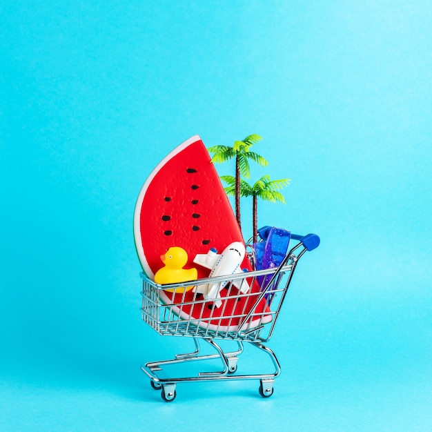 Foto conceito de praia tropical feito com coisas de verão em carrinho de compras sobre fundo azul.