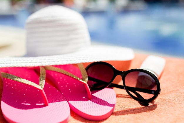 conceito de praia, verão e férias - close-up de chapéu, chinelos, protetor solar e óculos de sol na piscina