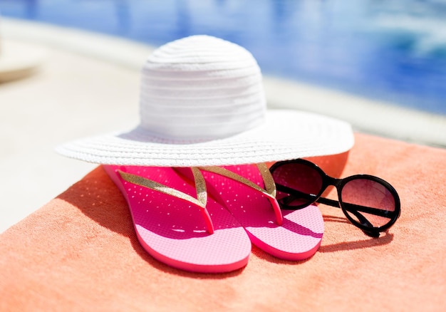 conceito de praia, verão, férias e acessórios - close-up de chapéu, chinelos e óculos de sol na piscina
