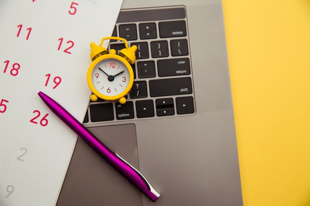 Foto conceito de prazo. laptop e despertador amarelo, calendário mensal em fundo amarelo. o tempo está fugindo.