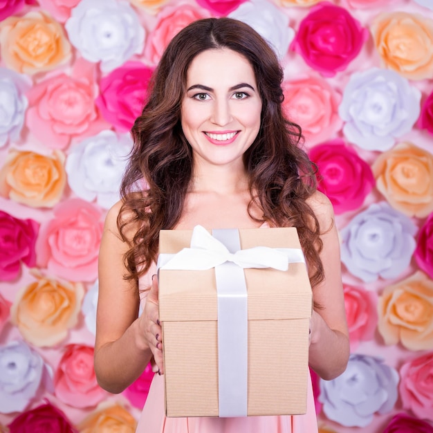 Foto conceito de primavera e feriados - retrato de uma jovem linda com caixa de presentes sobre fundo de flores coloridas