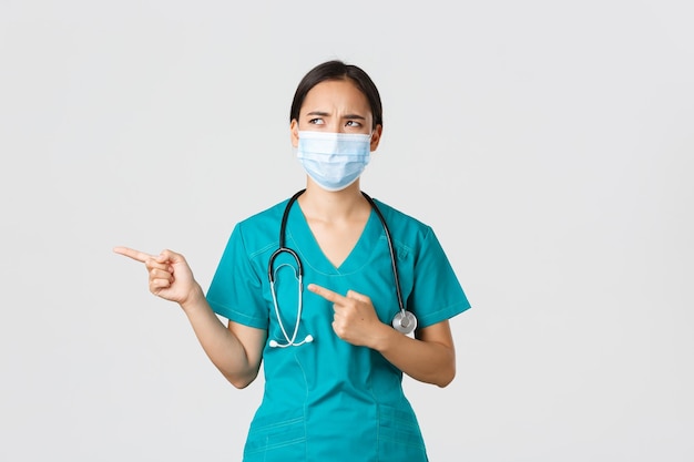 Conceito de profissionais de saúde da doença de coronavírus Covid19 Enfermeira asiática cética e desapontada em jaleco e máscara médica parecendo aversão descontente apontando para a esquerda