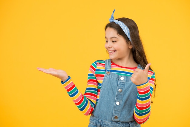 Conceito de propaganda. Promoção de produtos para crianças. Produto de lançamento. Apresentação do produto. Garoto feliz rosto sorridente mostrar algo no fundo amarelo do espaço da cópia da palma da mão aberta. Garota demonstrar produto.