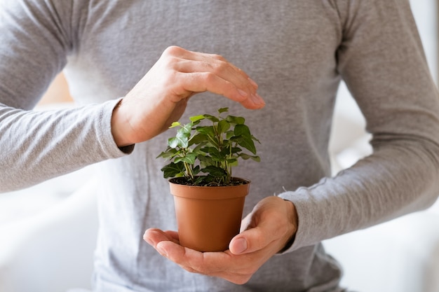 Conceito de proteção da natureza. Dia da Terra. Homem cobrindo a planta de casa com a mão.