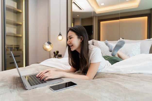 Conceito de quarto na cama confortável de uma adolescente do sexo feminino com seus dispositivos eletrônicos, o laptop e o smartphone.