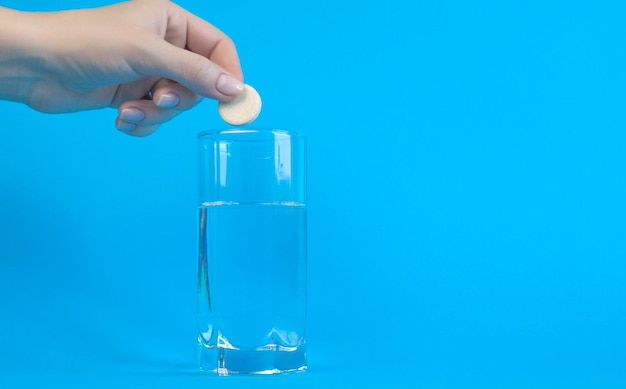 Conceito de recuperação A mão de uma mulher joga uma pílula efervescente em um copo de água em um fundo azul Lugar para texto