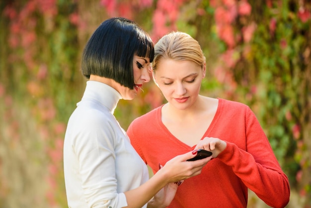 Conceito de redes sociais. Compartilhando link. Compre online. Tecnologia moderna. Surfando na internet. Comunicação online. Duas mulheres com smartphone se comunicando ao ar livre. Meninas se comunicando olhando para o telefone.