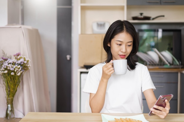 Conceito de relaxamento em casa Jovem mulher bebendo café e surfando nas mídias sociais no smartphone em casa