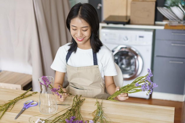 Conceito de relaxamento em casa jovem mulher sentada na cozinha e arranjar flores em um vaso na mesa