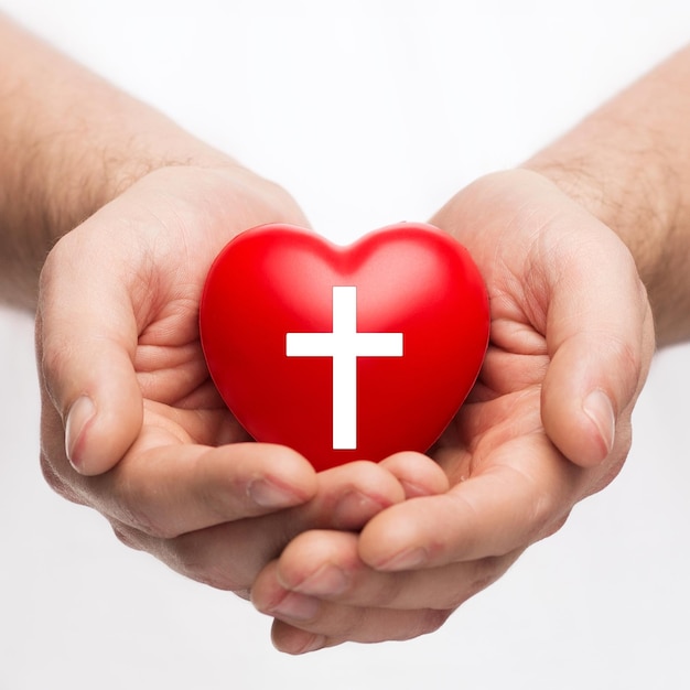 conceito de religião, cristianismo e caridade - mãos masculinas segurando um coração vermelho com o símbolo da cruz cristã