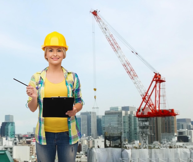 conceito de reparação, construção, construção e manutenção - mulher sorridente no capacete com prancheta fazendo anotações