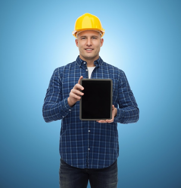 Conceito de reparação, construção, construção, pessoas e manutenção - sorridente construtor masculino ou trabalhador manual no capacete mostrando a tela em branco do computador tablet pc sobre fundo azul