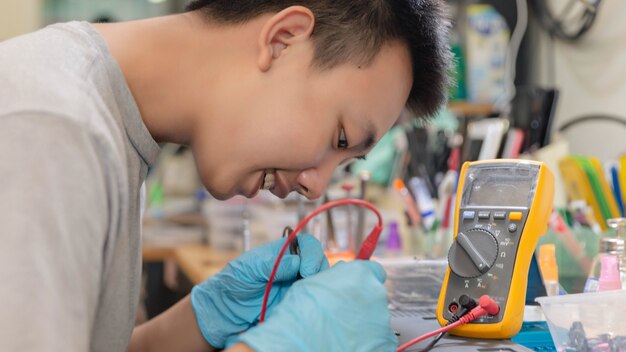 Conceito de reparo do telefone um jovem técnico em eletricidade usando um amperímetro que mede a corrente em um circuito de um dispositivo eletrônico.