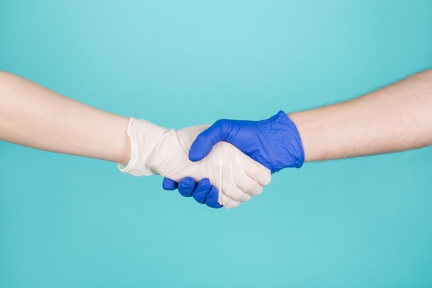 Conceito de reunião médico e paciente. conceito. foto recortada em close-up de uma mulher e um homem usando luvas se cumprimentando apertando as mãos, isoladas em um fundo branco azul turquesa