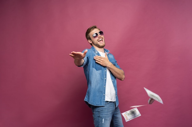 Conceito de riqueza financeira, prosperidade e ganhos na loteria - homem jogando fora seu dinheiro isolado sobre fundo rosa
