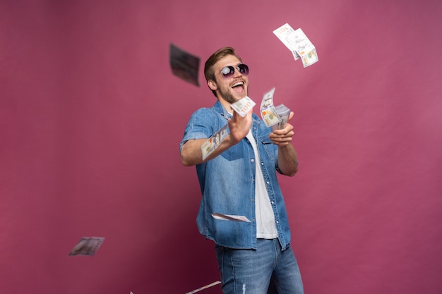 Conceito de riqueza financeira, prosperidade e ganhos na loteria - homem jogando fora seu dinheiro isolado sobre fundo rosa