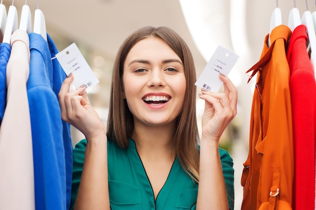 conceito de roupas, moda, venda e pessoas - mulher feliz mostrando etiquetas de preço em roupas em shopping center ou shopping