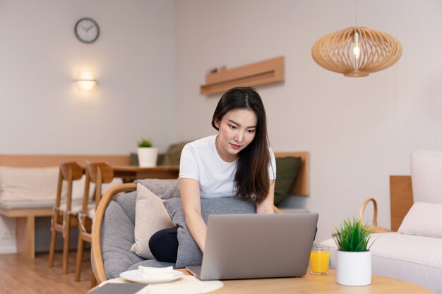 Conceito de sala de estar no café uma garota com um coque usando seu laptop indo na internet com um copo de suco de laranja.