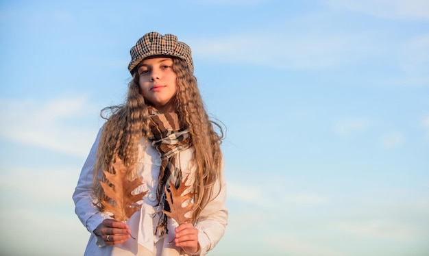 Conceito de salão de cabeleireiro menina pequena com cabelo encaracolado criança segura folha de outono menina elegante no outono boina tendências de outono moda criança olhar céu claro tempo feliz infância espaço de cópia