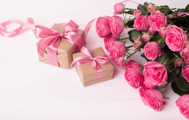 Conceito de São Valentim. Rosas cor de rosa e caixas de presente com fitas na mesa de madeira branca.