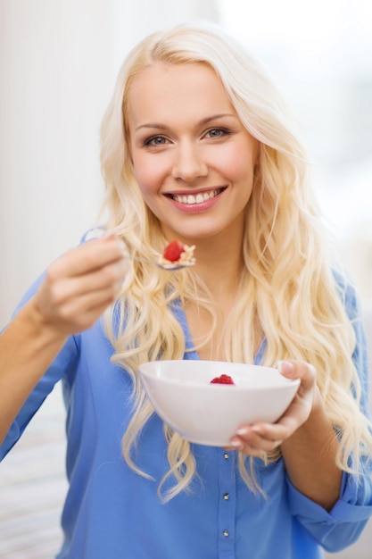 conceito de saúde, comida, casa e felicidade - mulher sorridente com tigela de muesli tomando café da manhã em casa
