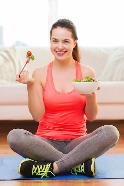 Foto conceito de saúde, dieta, lar e felicidade - adolescente esportiva sorridente com salada verde em casa