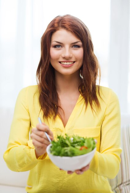 Conceito de saúde, dieta, lar e felicidade - jovem sorridente com salada verde em casa