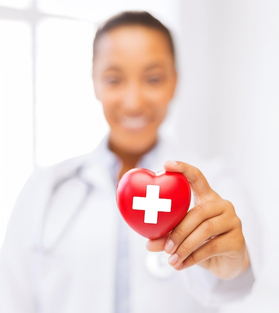 Foto conceito de saúde e medicina - médica afro-americana segurando coração com símbolo da cruz vermelha