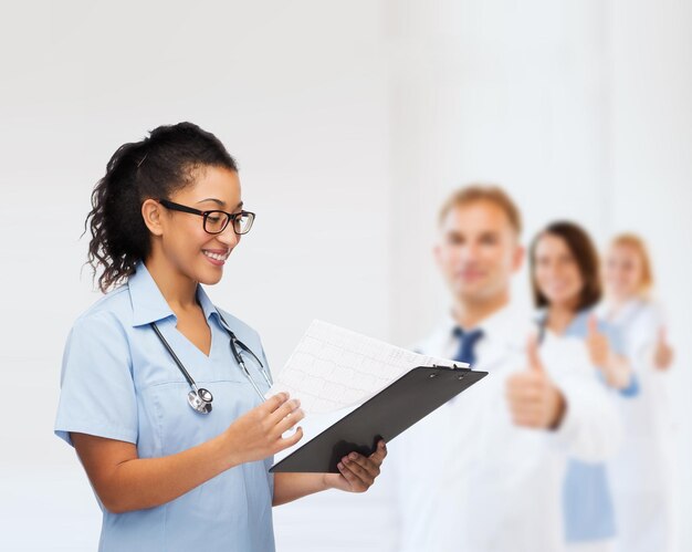 Foto conceito de saúde e medicina - médica afro-americana sorridente ou enfermeira em óculos com estetoscópio e prancheta