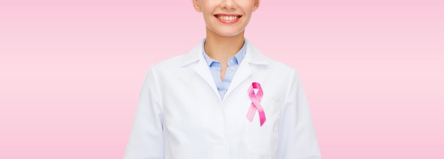 Conceito de saúde e medicina - médica sorridente com fita rosa de conscientização do câncer sobre fundo rosa