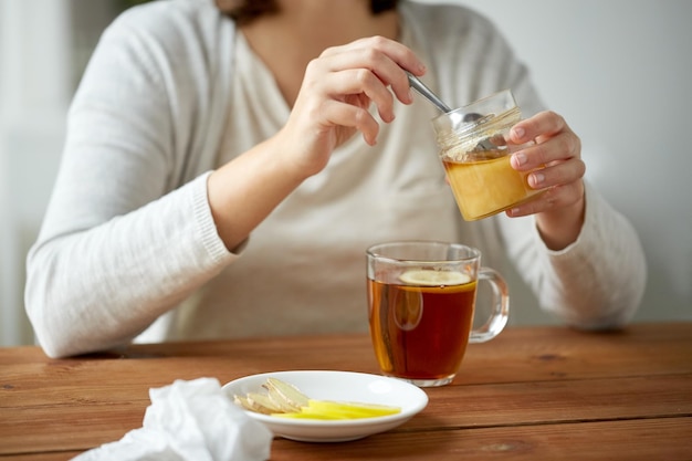 Foto conceito de saúde, medicina tradicional e etnociência - close-up da mulher adicionando mel ao chá com limão