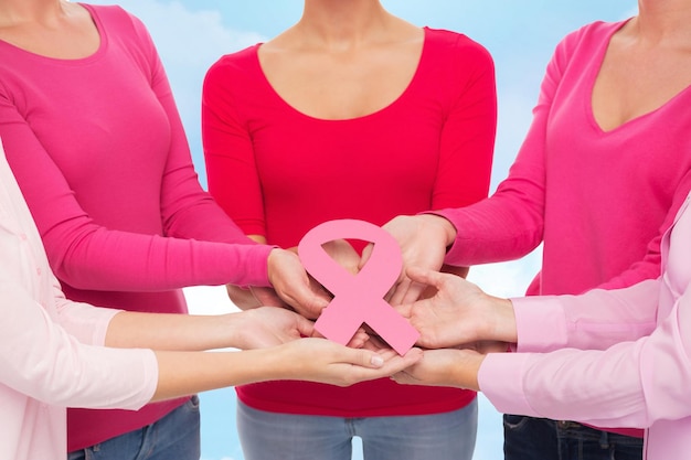 Foto conceito de saúde, pessoas e medicina - close-up de mulheres em camisas em branco com fita rosa de conscientização de câncer de mama sobre fundo de céu azul