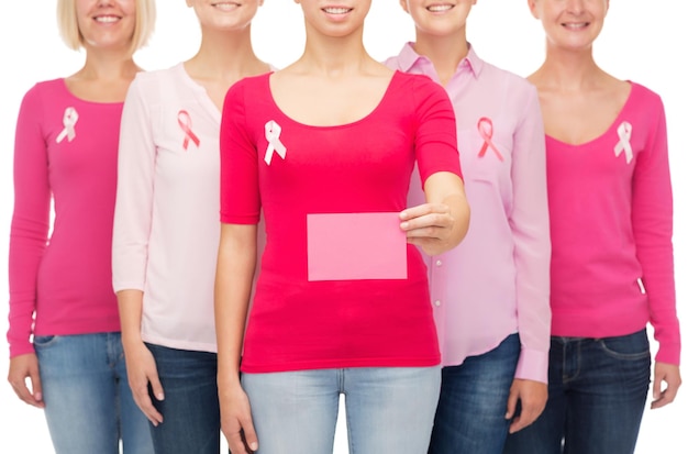 Foto conceito de saúde, pessoas e medicina - close-up de mulheres sorridentes em camisas com fitas de conscientização de câncer de mama rosa e cartão de papel em branco sobre fundo branco