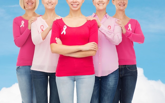 Foto conceito de saúde, pessoas e medicina - close-up de mulheres sorridentes em camisas em branco com fitas de conscientização de câncer de mama rosa sobre céu azul e fundo de nuvem branca