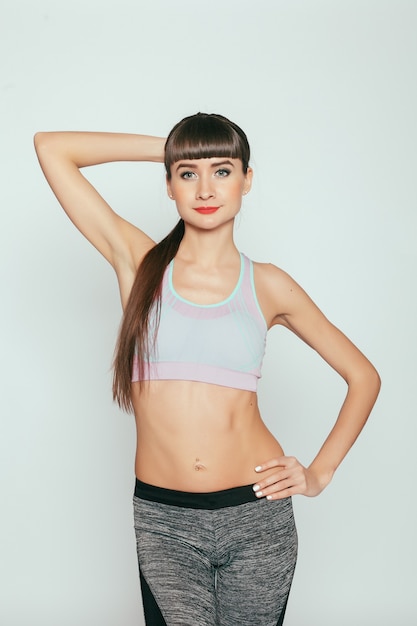 Conceito de saúde, pessoas, esporte e estilo de vida - garota jovem feliz fitness com corpo desportivo no estúdio em um fundo cinza. Belo ajuste menina. Modelo de fitness em sportswear cinza. Estilo de vida saudável.