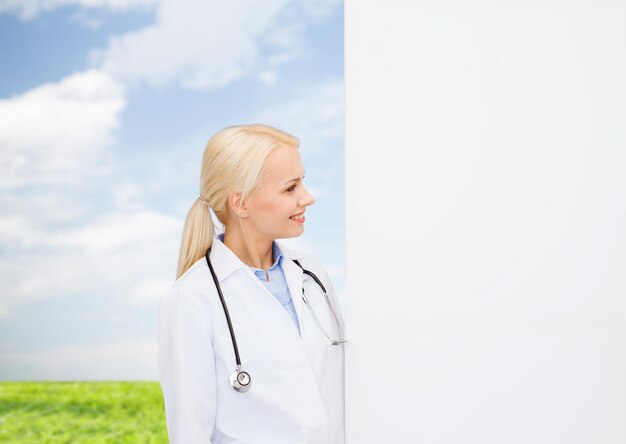 Foto conceito de saúde, propaganda, pessoas e medicina - médica sorridente com estetoscópio olhando para algo sobre fundo natural