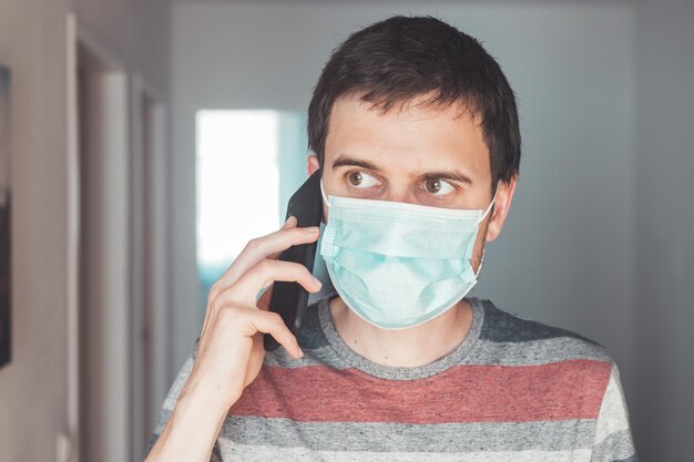 Conceito de segurança contra gripe e corona Homem usando máscara facial para se proteger e usando telefone celular dentro de casa