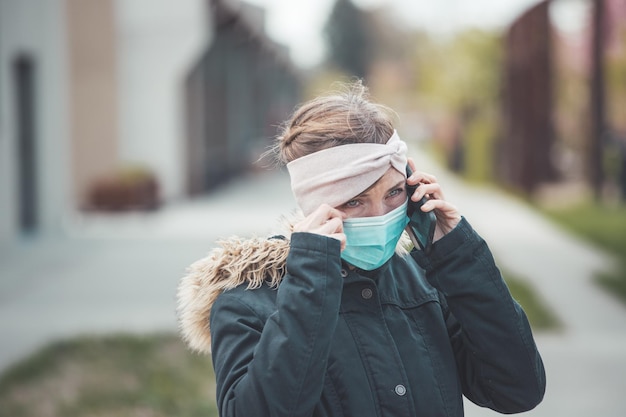 Foto conceito de segurança contra gripe e corona mulher usando máscara facial para se proteger e usando smartphone ao ar livre