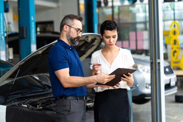 Conceito de seguro automóvel. O agente de seguros examina o carro danificado com as informações escritas do cliente no formulário de relatório de sinistro.