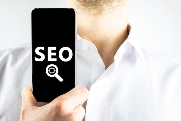 Conceito de SEO para smartphoneEmpresário segurando smartphone com abreviação de SEO e símbolos de configuração