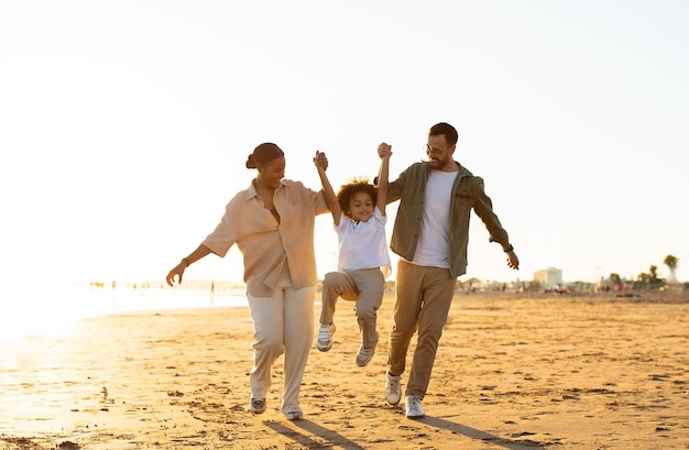 Conceito de serenidade à beira-mar feliz família multirracial caminhando ao longo da costa pais levantando filho