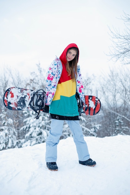 Foto conceito de snowboard ao ar livre do inverno da mulher. mulher jovem segurando snowboard nos ombros, ela está desviando o olhar e sorrindo, copie o espaço, close-up