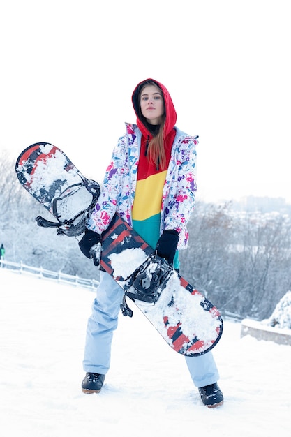 Conceito de snowboard ao ar livre do inverno da mulher. Mulher jovem segurando snowboard nos ombros, ela está desviando o olhar e sorrindo, copie o espaço, close-up