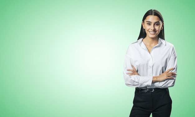 Conceito de sucesso comercial com jovem sorridente, dobrando as mãos na camisa branca e calça preta em fundo em branco verde claro abstrato com lugar para o seu logotipo ou texto Mock up