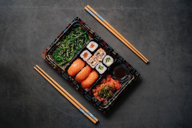 Conceito de sushi para viagem. Caixa de coleta com sushi. Com rolos de sushi e pauzinhos. Maki. Sashimi. Salmão. Atum. Wasabi. Asiático. Japonês.