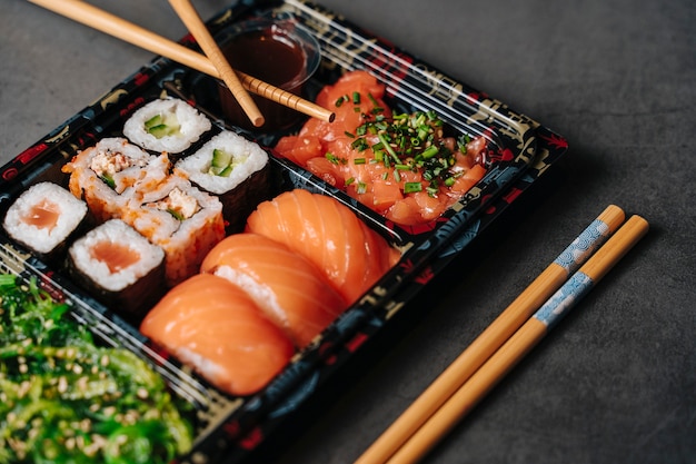 Conceito de sushi para viagem. Caixa de coleta com sushi. Com rolos de sushi e pauzinhos. Maki. Sashimi. Salmão. Atum. Wasabi. Asiático. Japonês.