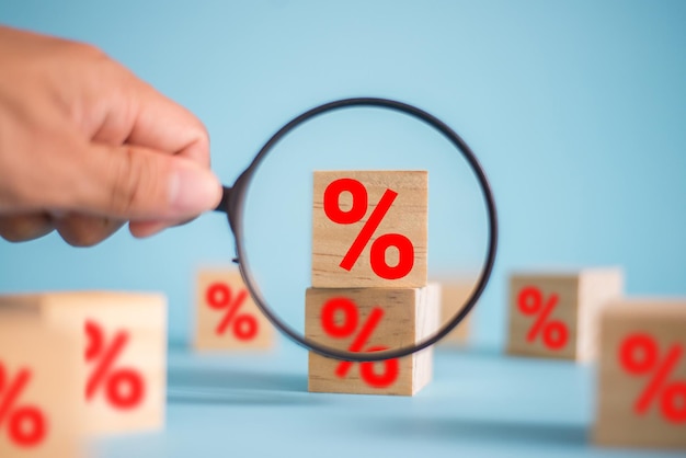 Foto conceito de taxas financeiras e de hipoteca de taxa de juros na mão de um empresário segurando uma lupa, escolha o bloco de cubo de madeira com símbolo de porcentagem de ícone no fundo azul