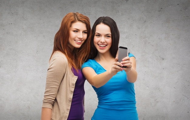 conceito de tecnologia, amizade e pessoas - dois adolescentes sorridentes tirando foto com a câmera do smartphone