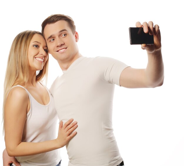 Conceito de tecnologia, amor e amizade sorrindo casal com smartphone, selfie e diversão. Estúdio disparado sobre fundo branco.