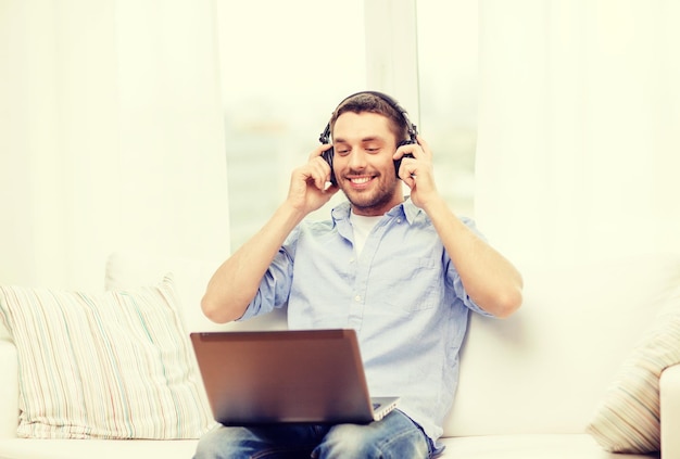 conceito de tecnologia, casa, música e estilo de vida - homem sorridente com laptop e fones de ouvido em casa